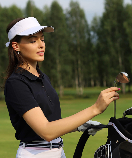 Yeşil golf sahasında arabadaki çantadan sopa seçen lacivert tişörtlü kadın.